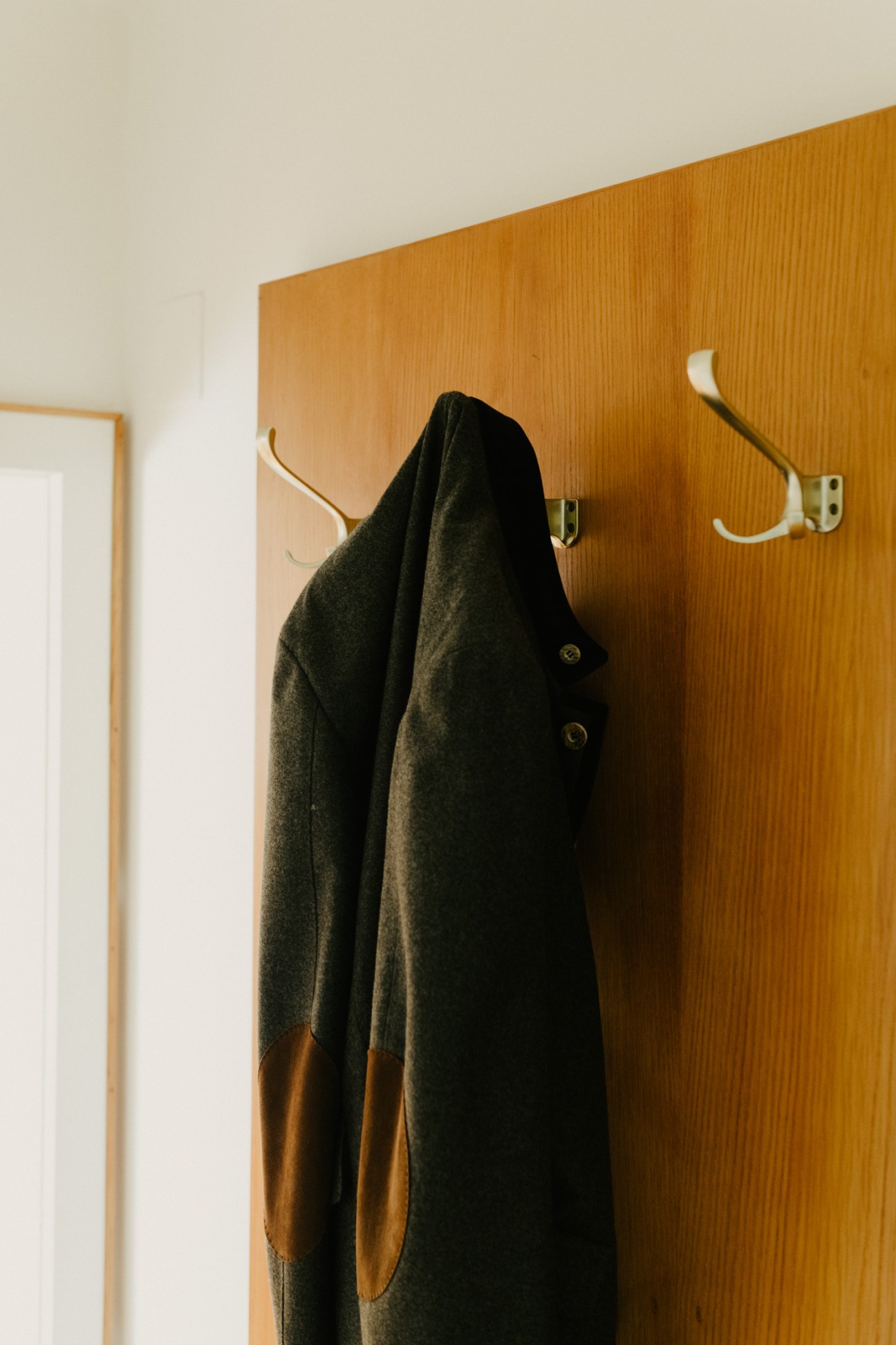 Dark wool coat with tan elbow patches hanging on wooden wall hooks.
