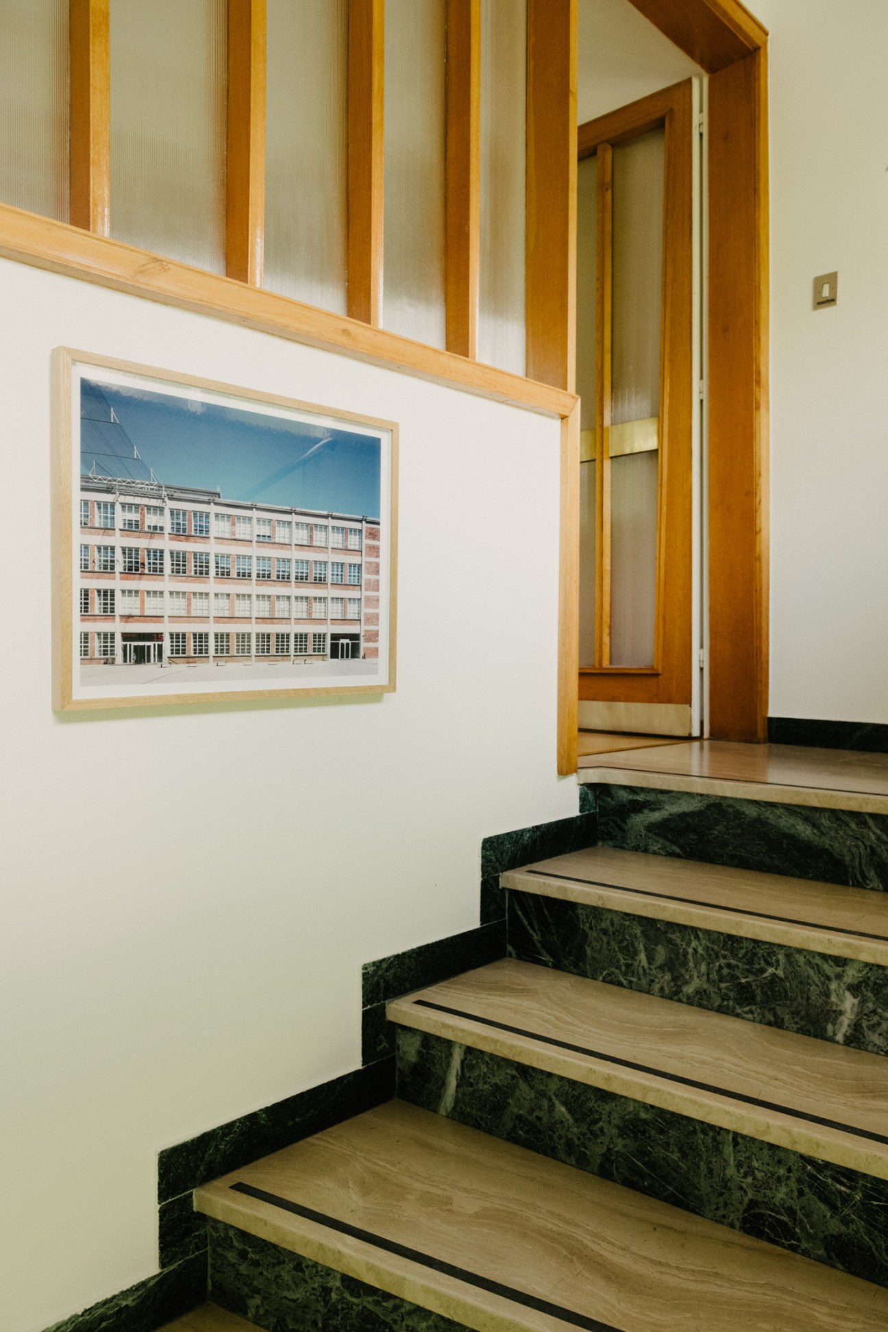 Wooden staircase with green marble risers and oak treads leading upward, with a framed architectural photograph on the wall.