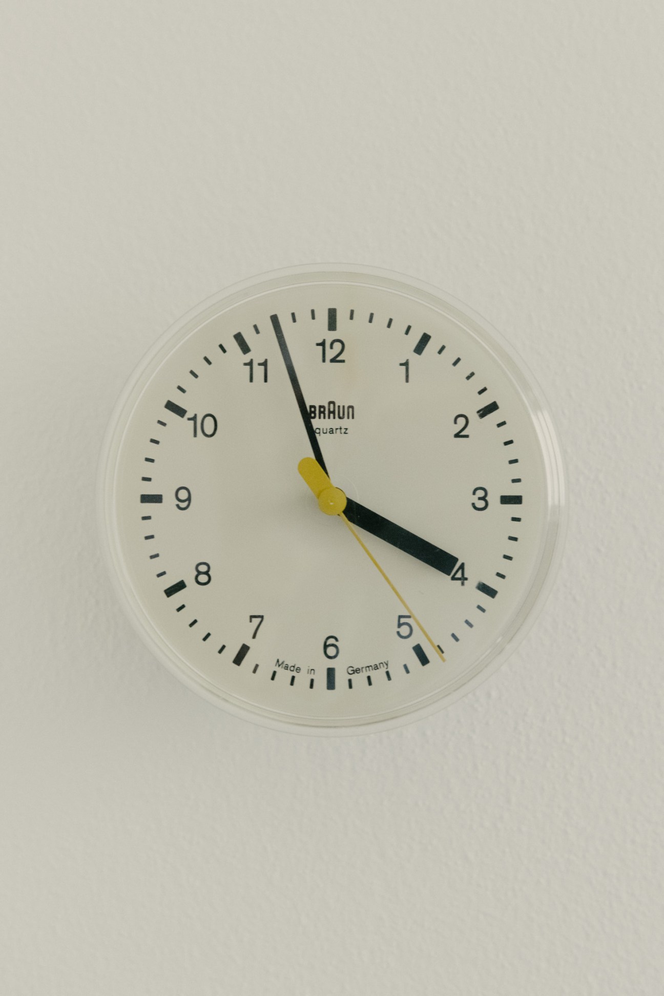 Dieter Rams-designed Braun quartz wall clock with cream face, black numerals and hands, mounted on a light grey wall.