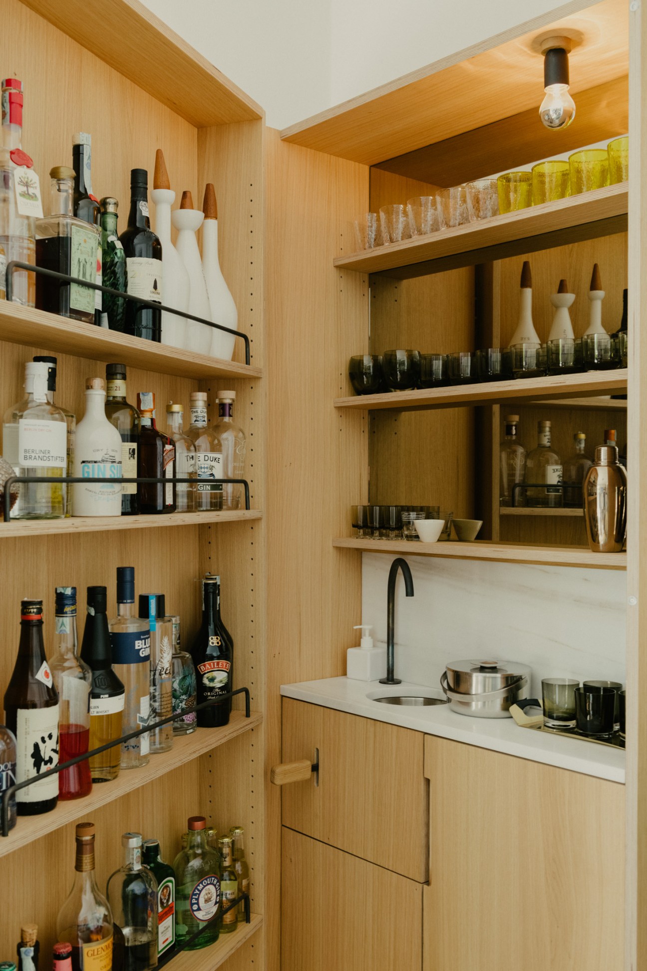 Custom-designed oak drinks cabinet with shelving displaying spirits and barware, featuring a built-in tap.
