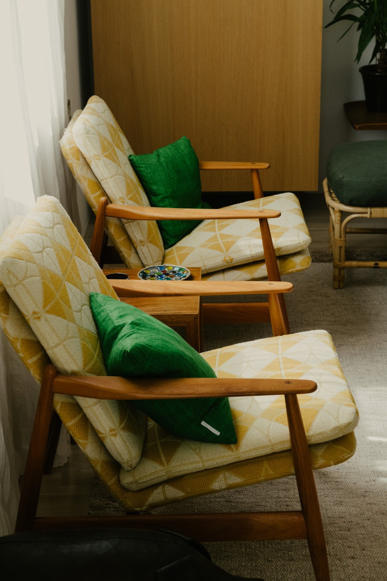 Mid-century wooden chairs with yellow and white patterned cushions and green pillows arranged in a living room.