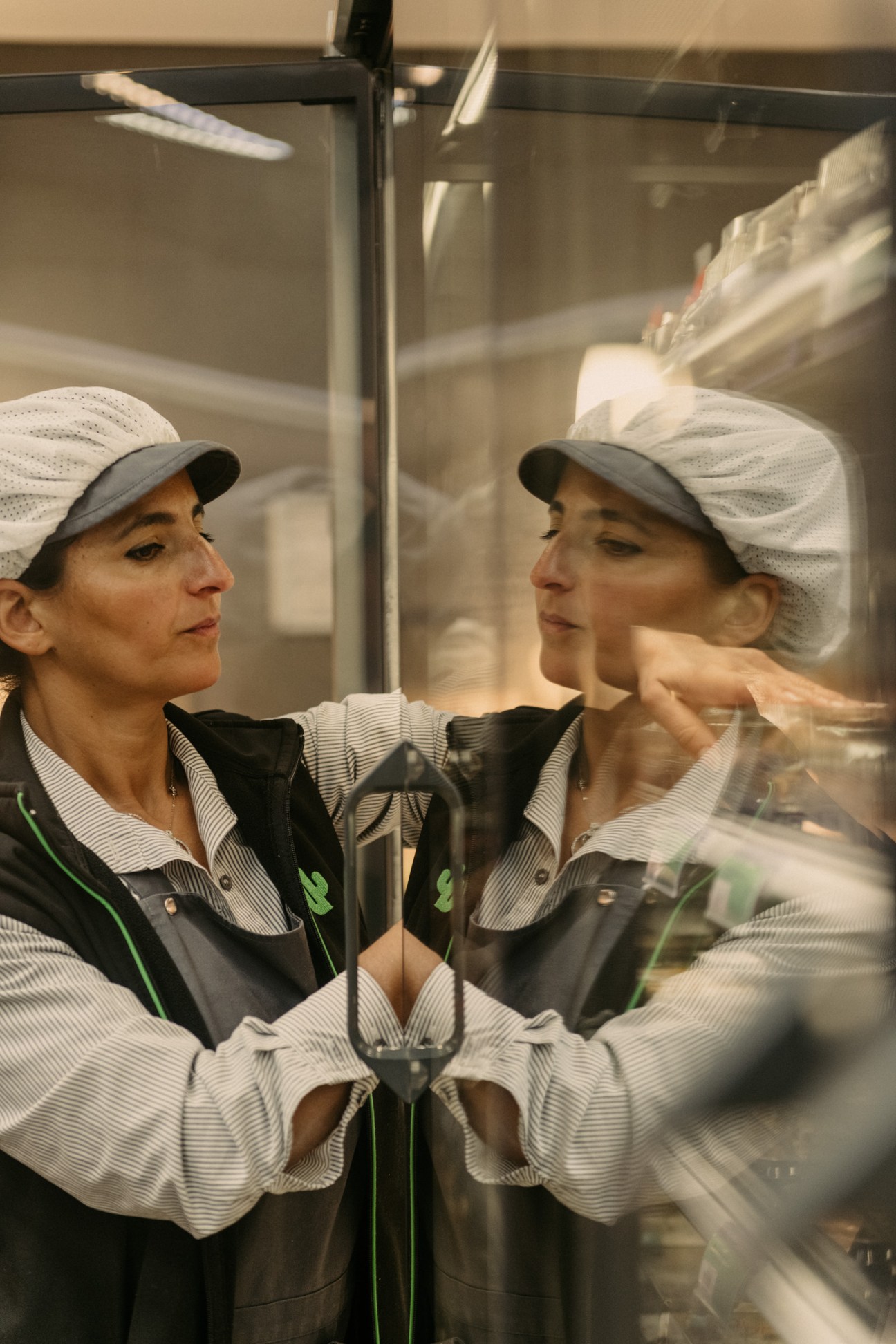 A Cactus supermarket staff member in uniform examining dairy products in a refrigerated display case.