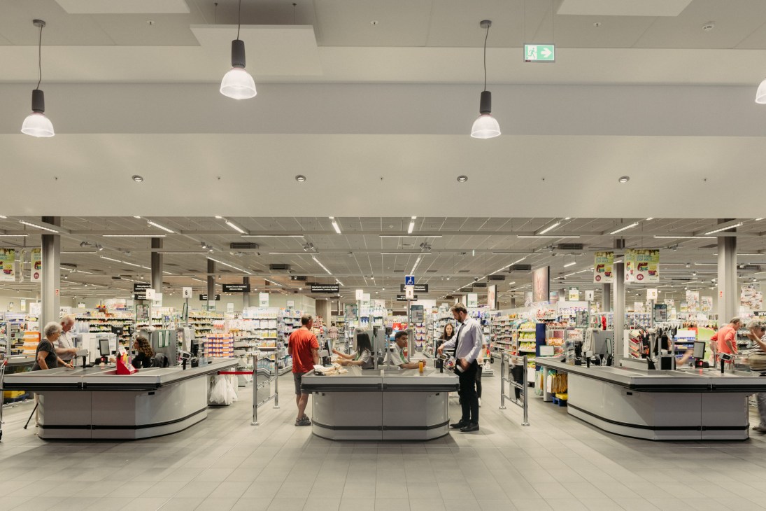 Interior of Cactus Howald supermarket showing checkout counters, shelves, and customers shopping in a modern grey and white store design.