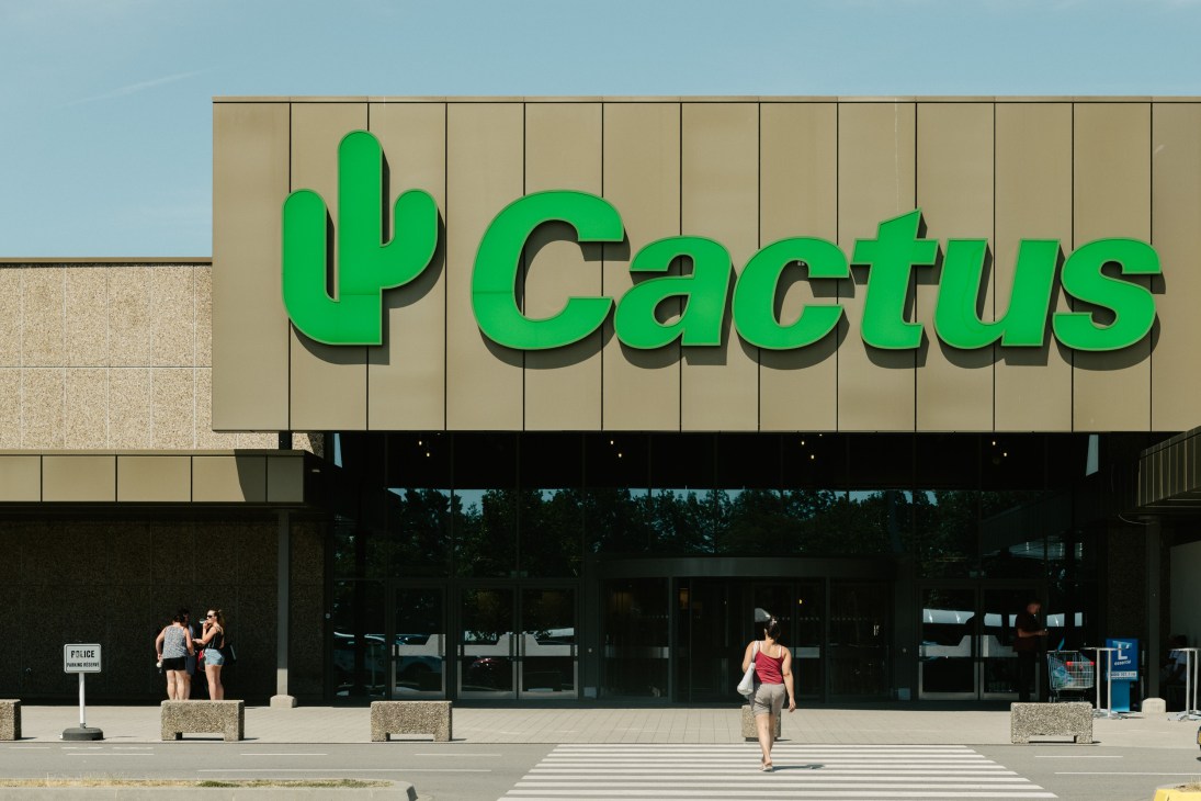 Exterior of Cactus supermarket storefront with large green cactus logo on beige facade and black entrance.