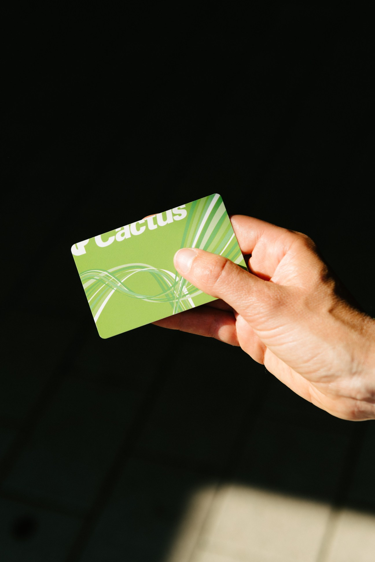 Hand holding a green Cactus loyalty card against a black background.