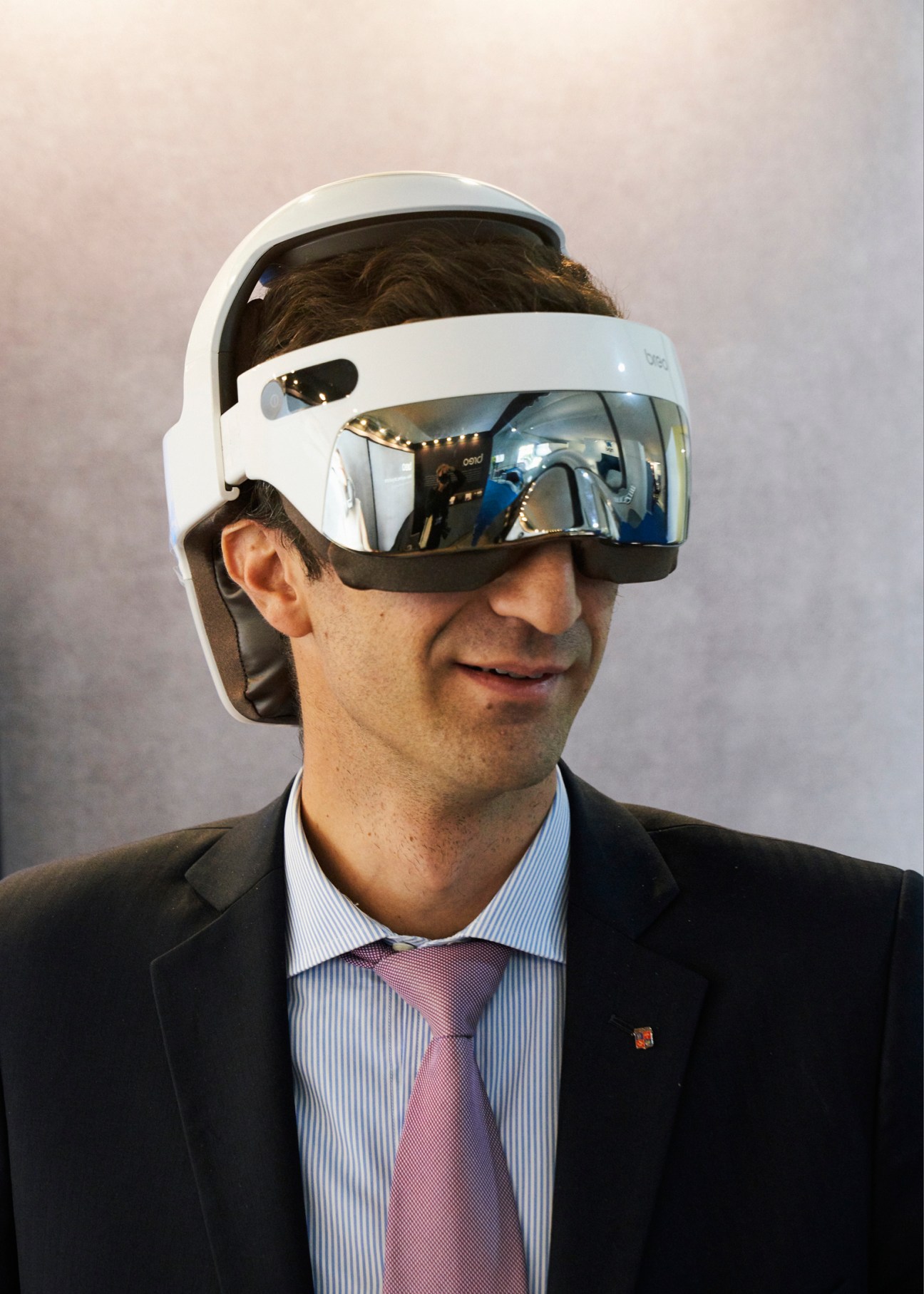 Man in business suit wearing white VR headset with reflective visor at trade show