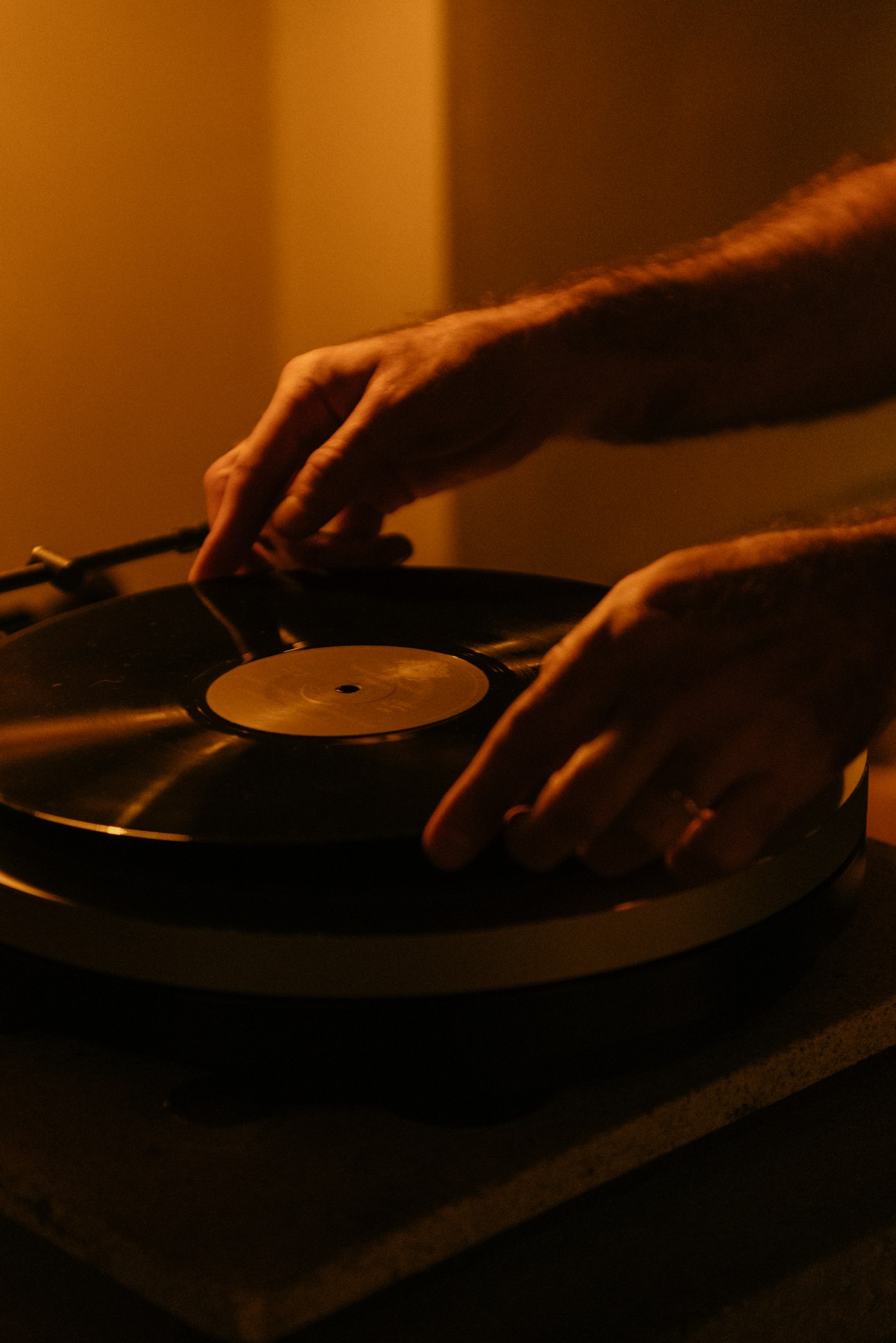 DJ's hands operating a Micro Seiki DQX-500 turntable in warm orange lighting.