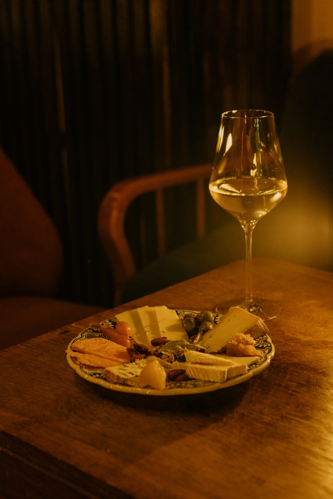 Glass of wine and cheese plate on wooden table in dimly lit bar.