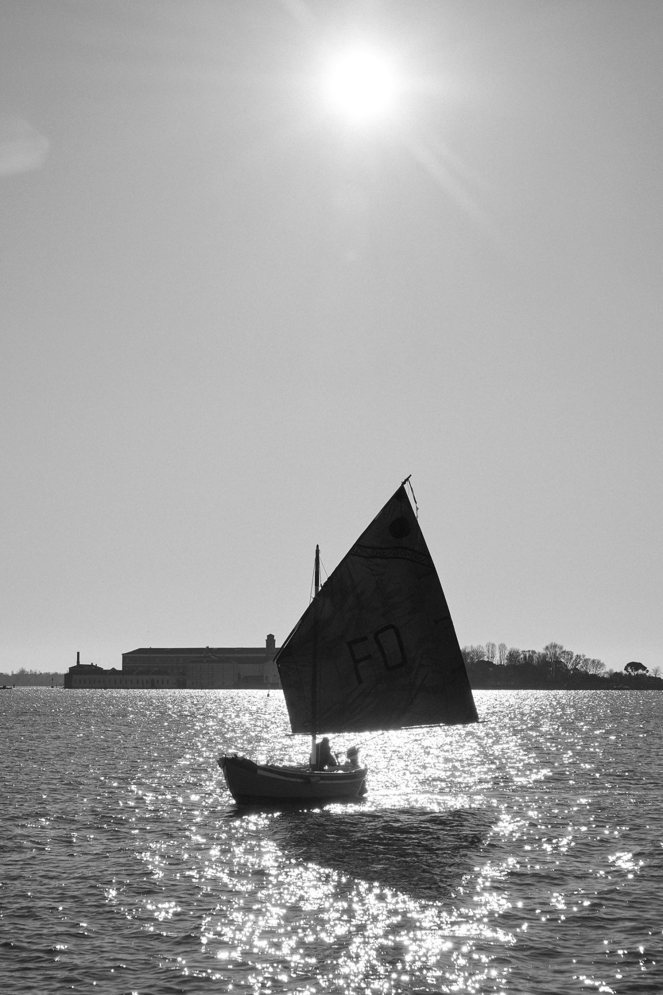Silhouetted sailboat with triangular sail on sparkling water against bright sky