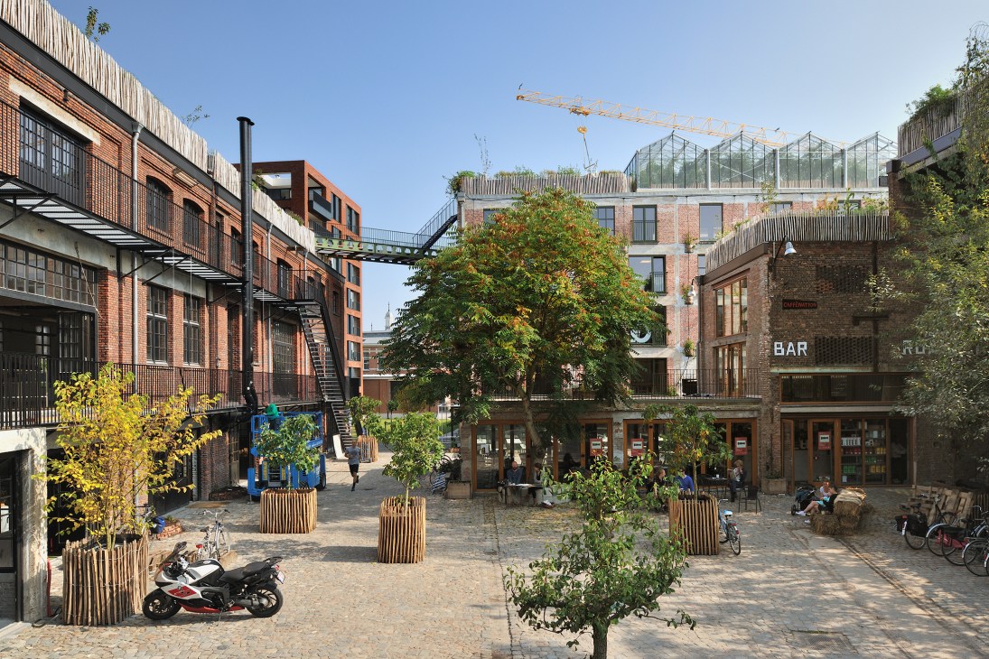 Pakt courtyard in Antwerp showing renovated brick buildings, rooftop greenhouses, and people moving between different business spaces