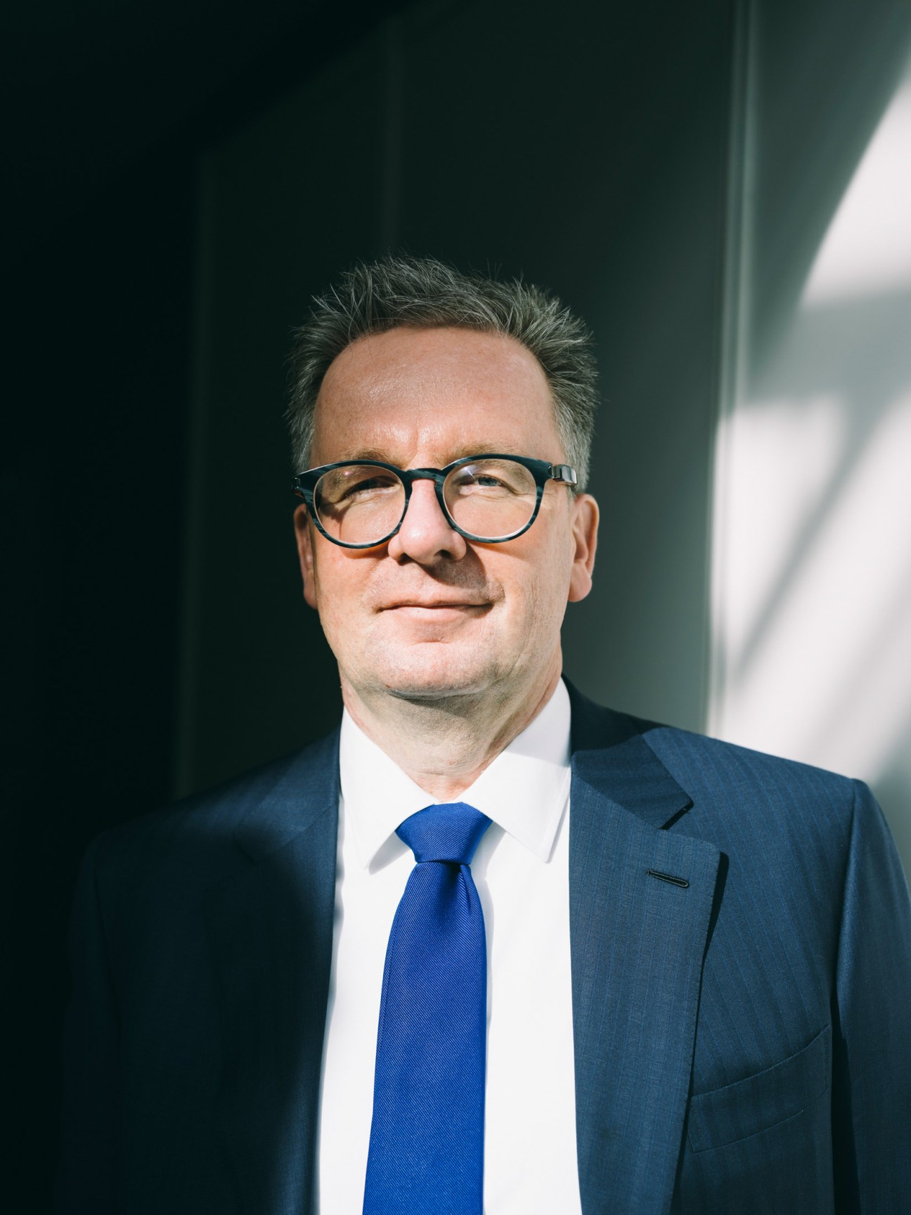 Michael Rauterkus, CEO of Grohe, wearing glasses and a blue tie against a dark green background.