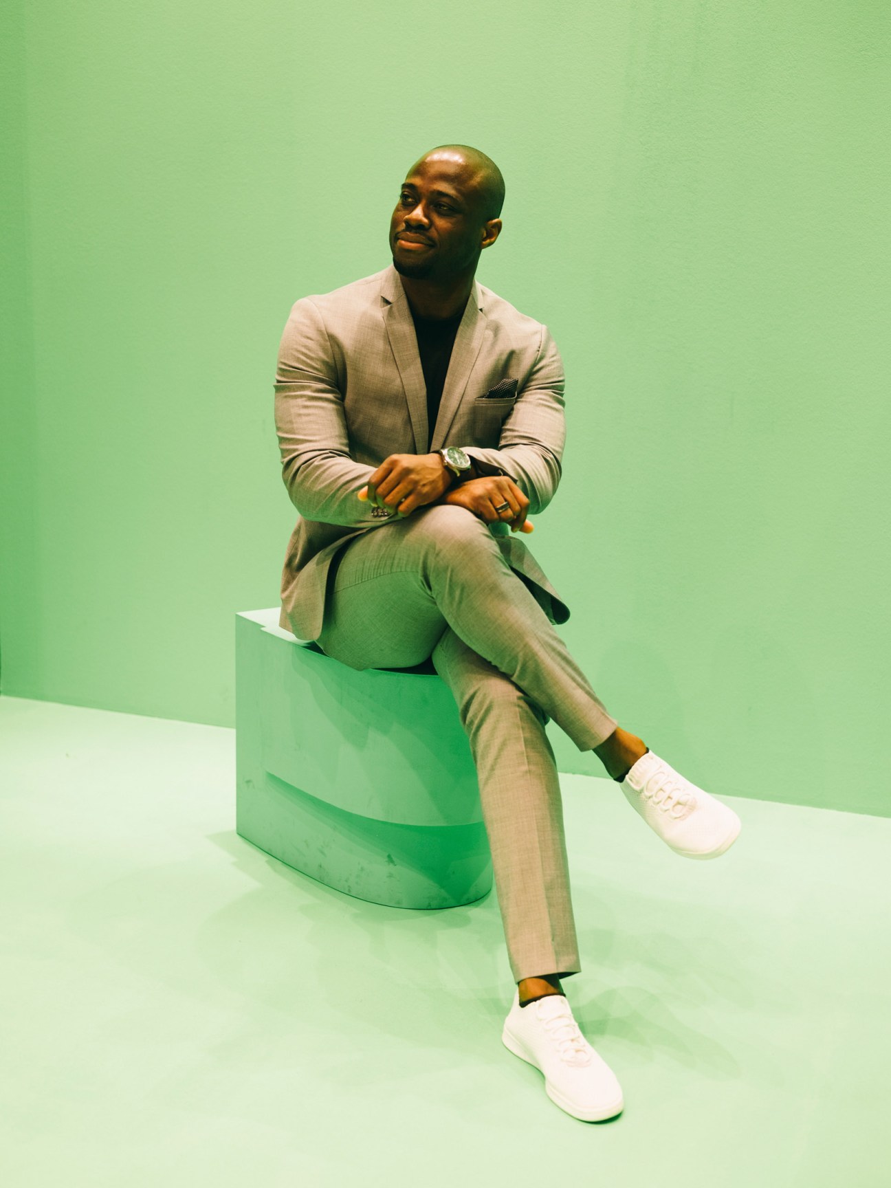 Man in beige suit sitting on a green modern toilet against a green background.