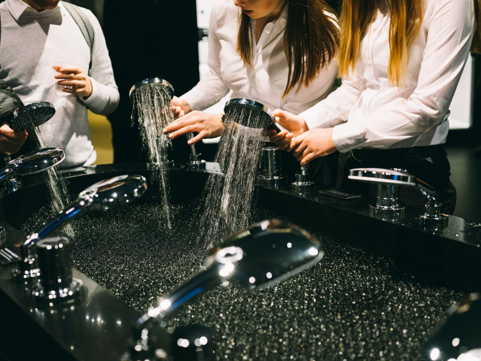 People in white shirts demonstrating water flowing from Grohe hand showers at a bathroom design fair.