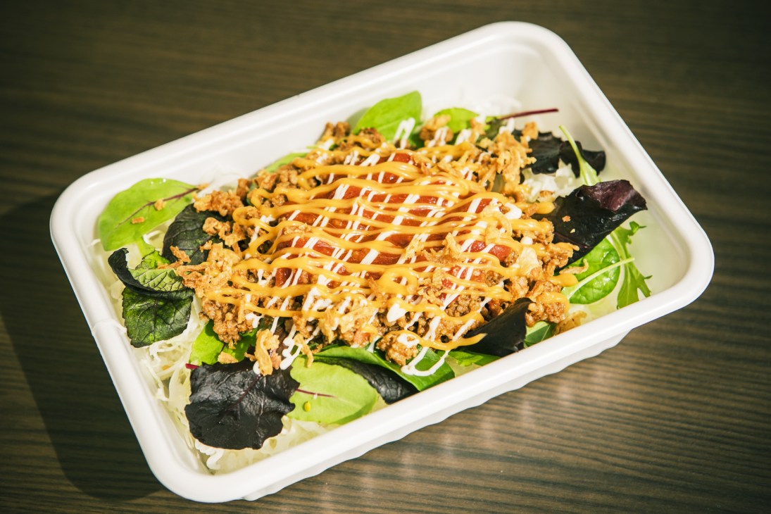 Okinawan taco rice served in a white container with seasoned ground meat, lettuce, nori, and creamy sauce drizzle.
