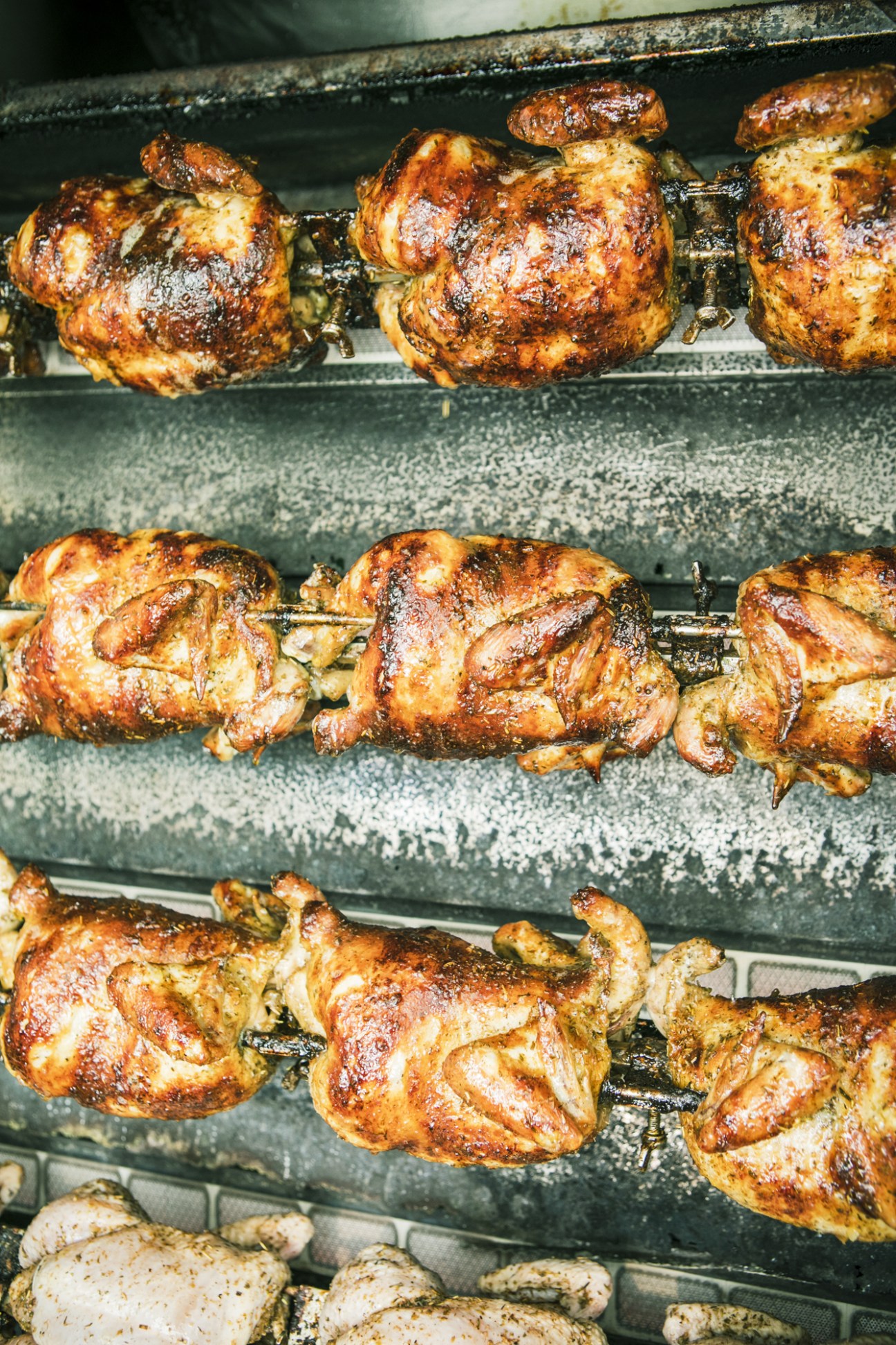Roasted chicken pieces cooking on a vertical rotisserie spit in a food truck kitchen.
