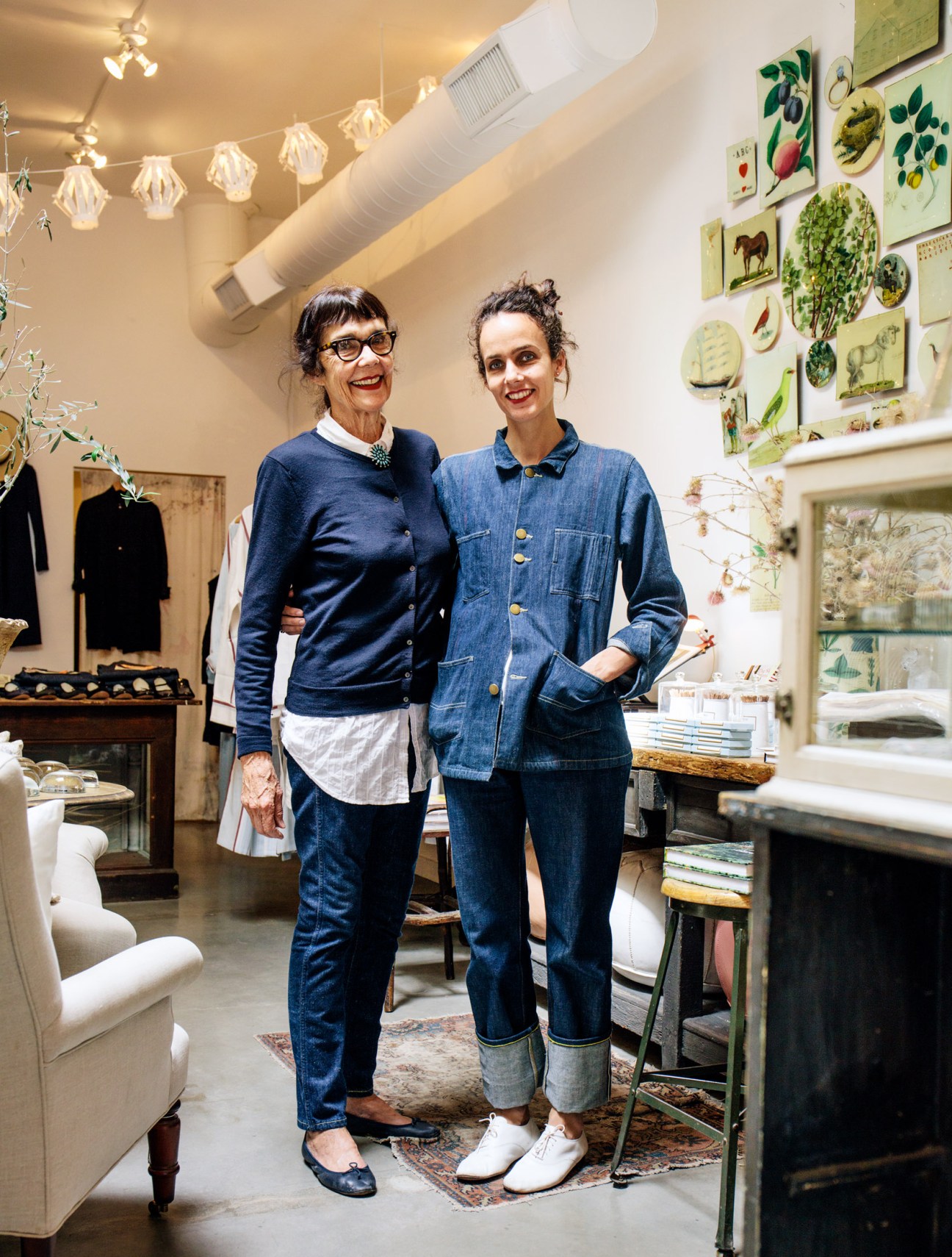 Bonnie and Crystal Flynt stand together in their Bon boutique shop, surrounded by clothing and botanical prints on the walls.