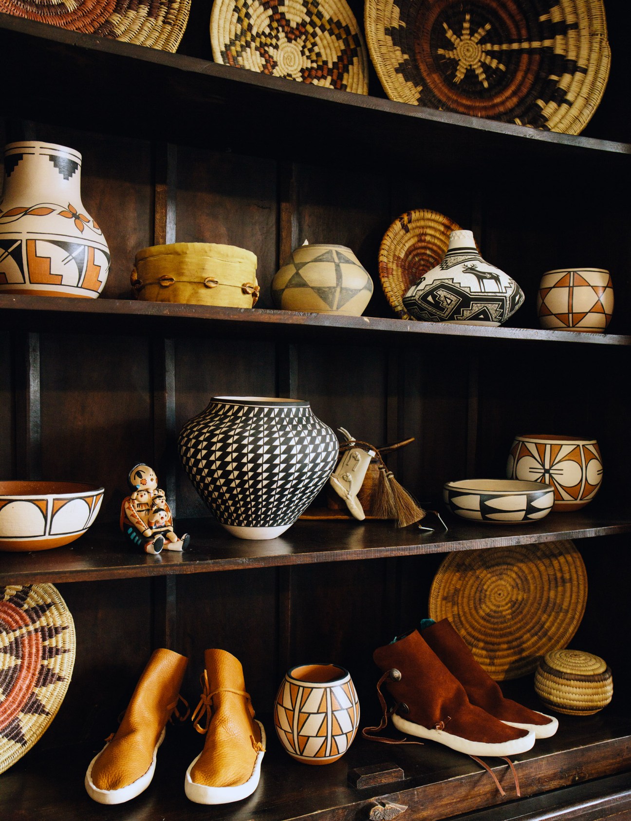Native American pottery, baskets and crafts displayed on dark wooden shelves.
