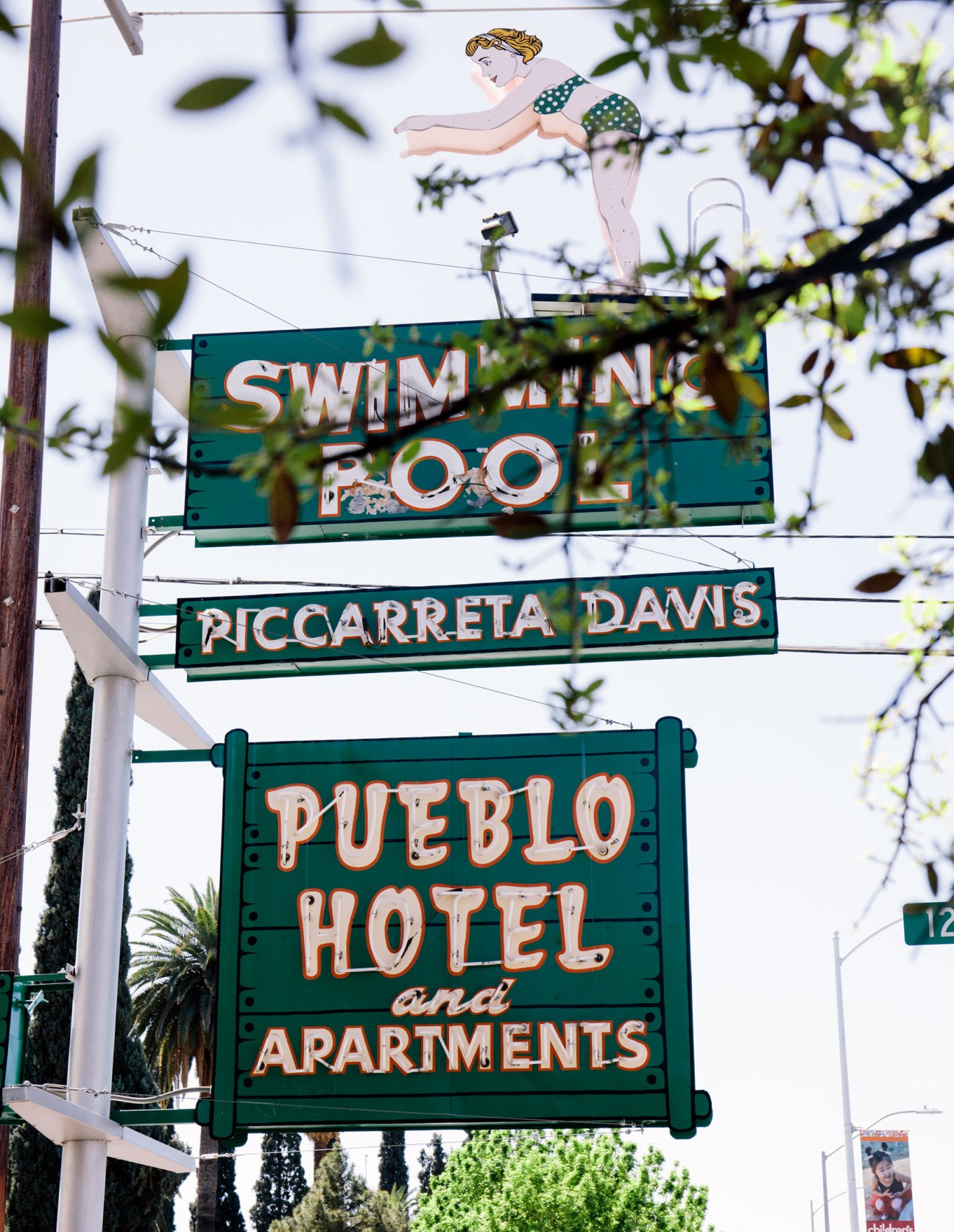 Vintage neon signs for Swimming Pool, Piccarreta Davis, and Pueblo Hotel and Apartments in Tucson with illustrated pin-up figure on top sign.