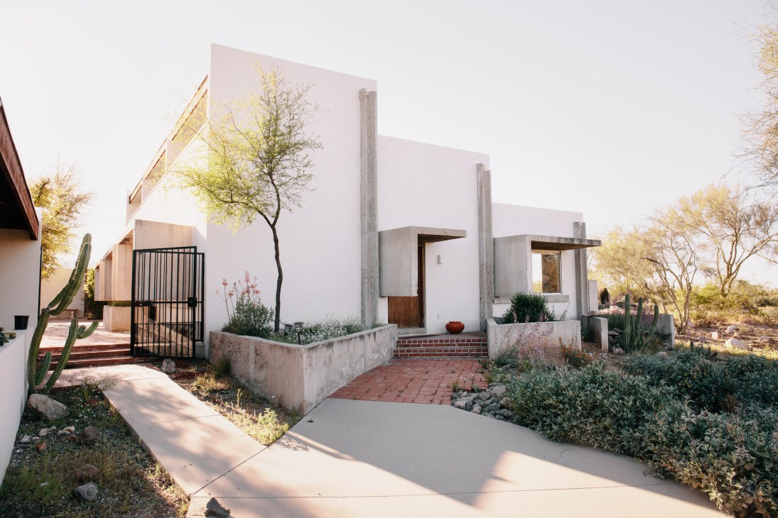Desert modernist house with white walls, concrete pillars, and desert landscaping including cacti.