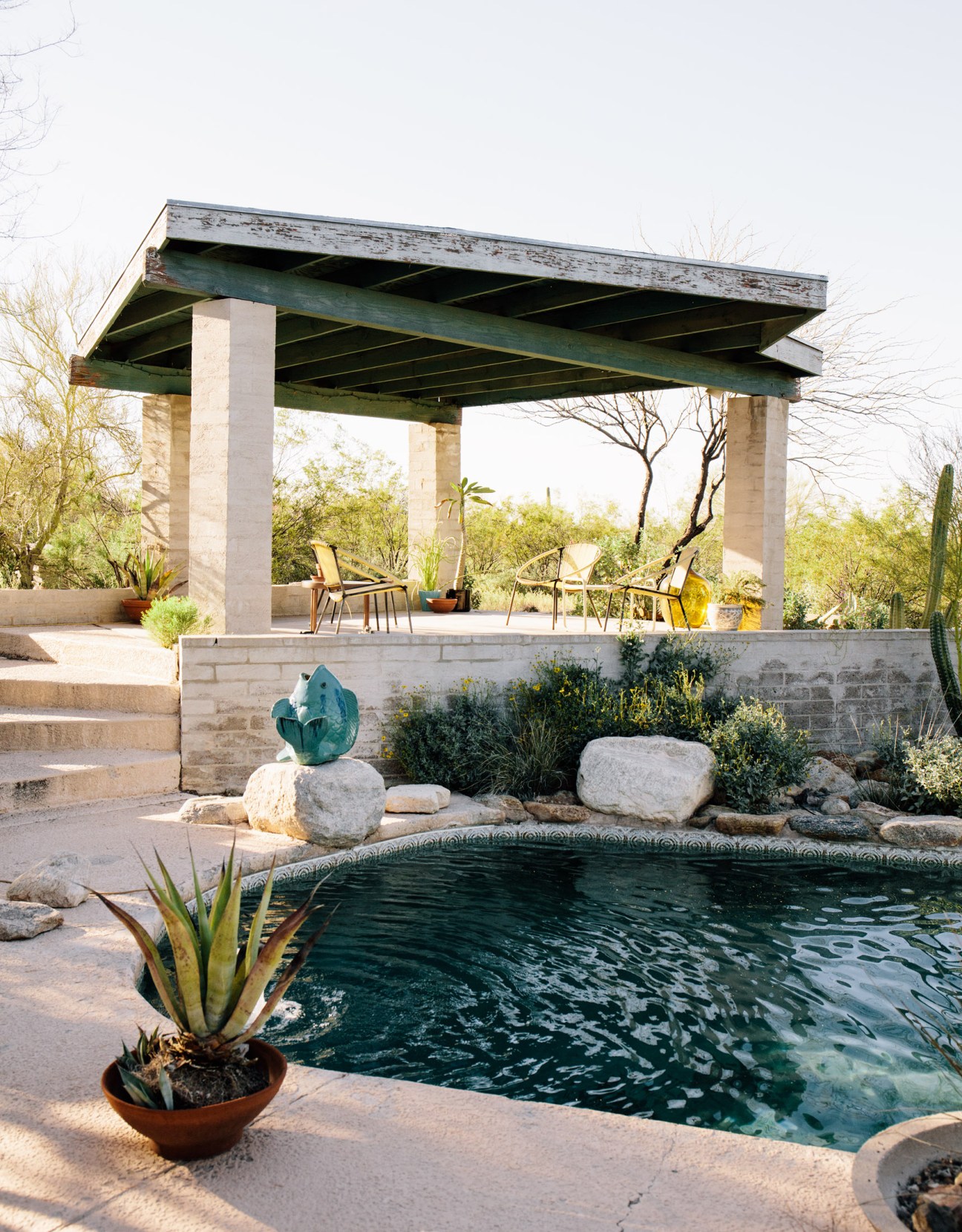 Desert modernist patio with cantilevered green pergola, pool, desert landscaping and mountain views.