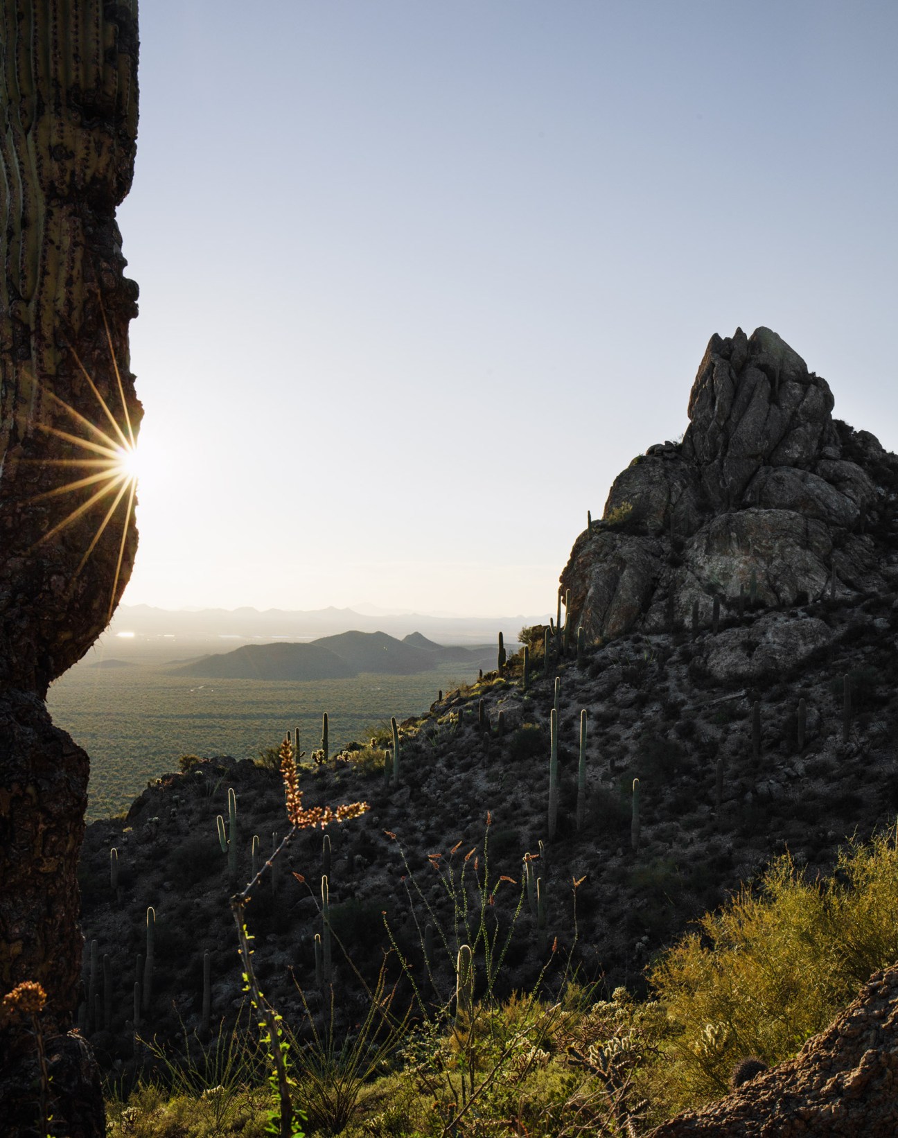 Sunset light breaks through desert rock formations framing saguaro cacti and mountains in the distance at Gates Pass.