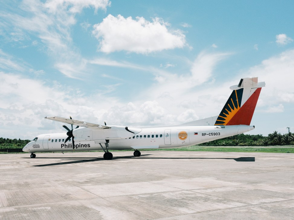 A Philippine Airlines turboprop aircraft parked on the tarmac at Siargao Airport under a blue sky with white clouds.