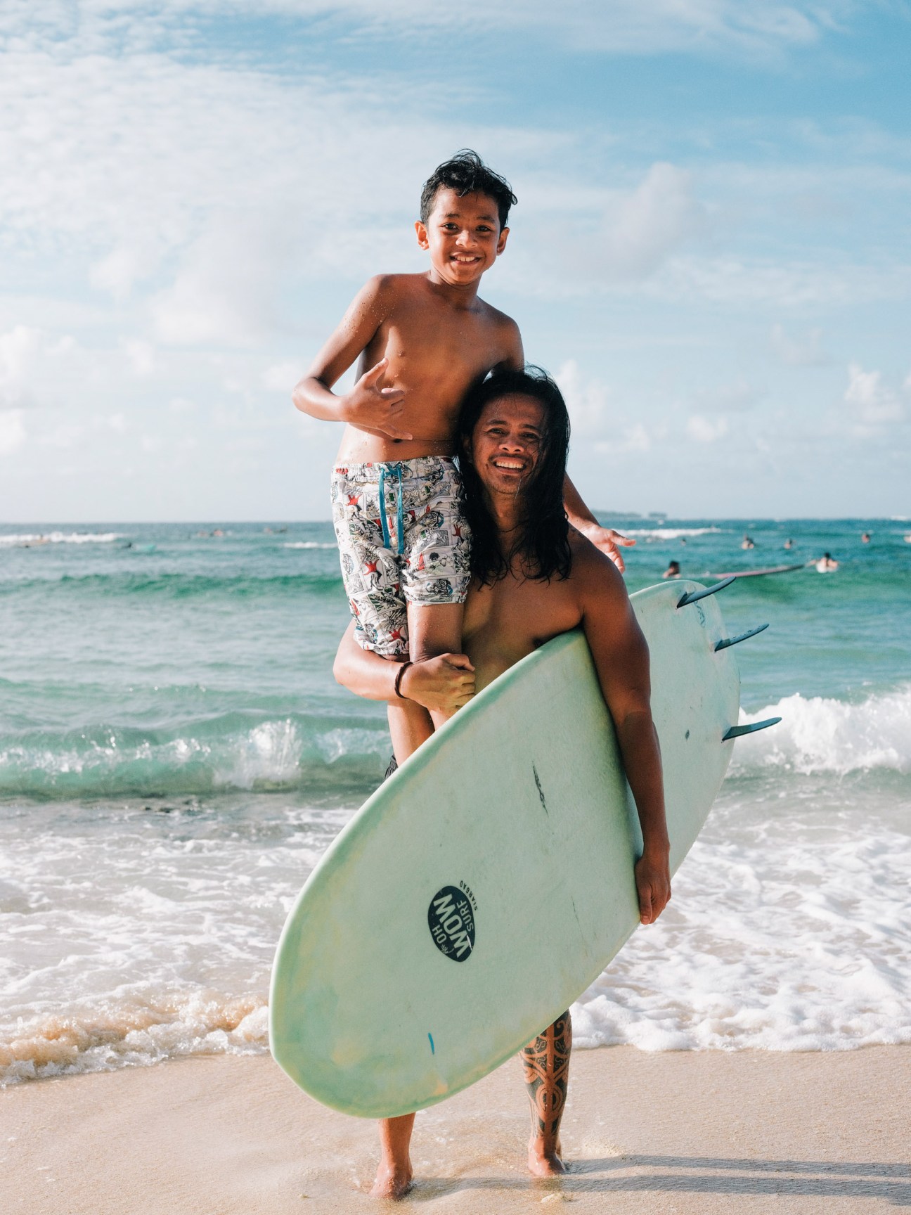 Surf instructor holding a young child on a surfboard in the ocean waves at Siargao beach.