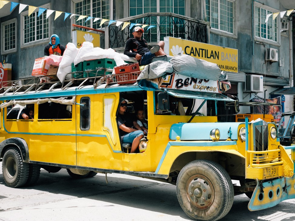 Colorful yellow and turquoise Jeepney tour bus loaded with passengers and cargo on a street in General Luna, Siargao.