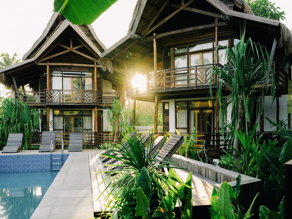 Bulan Villas resort with wooden bungalows, tropical plants, lounge chairs, and swimming pool at sunset.