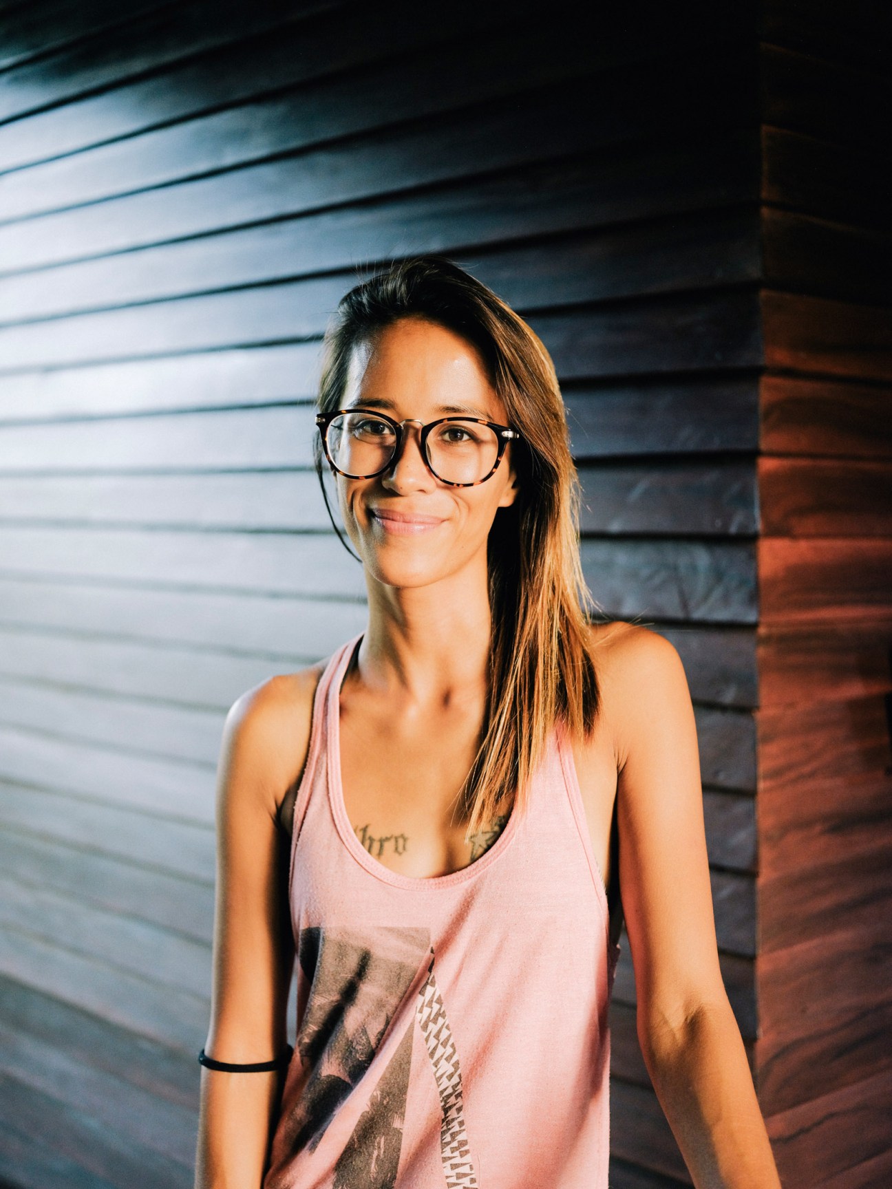 Abi Ponio-Quadelli wearing glasses and a pink tank top standing against a striped wall.