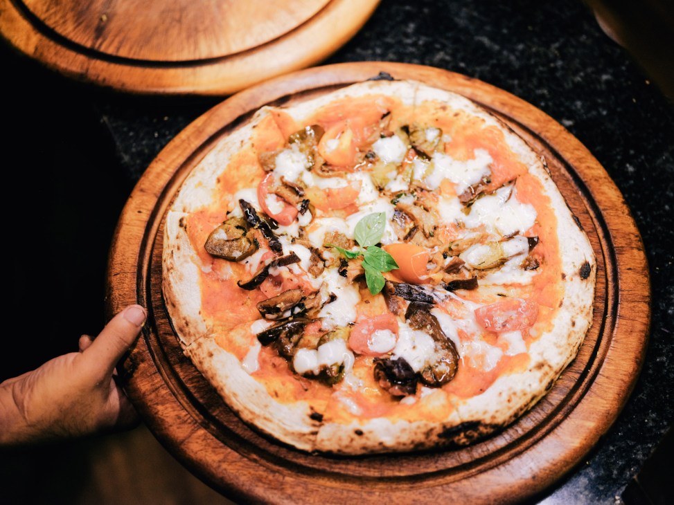 Pizza with salmon, mushrooms, mozzarella and herbs on wooden board at Bulan Villas resort.