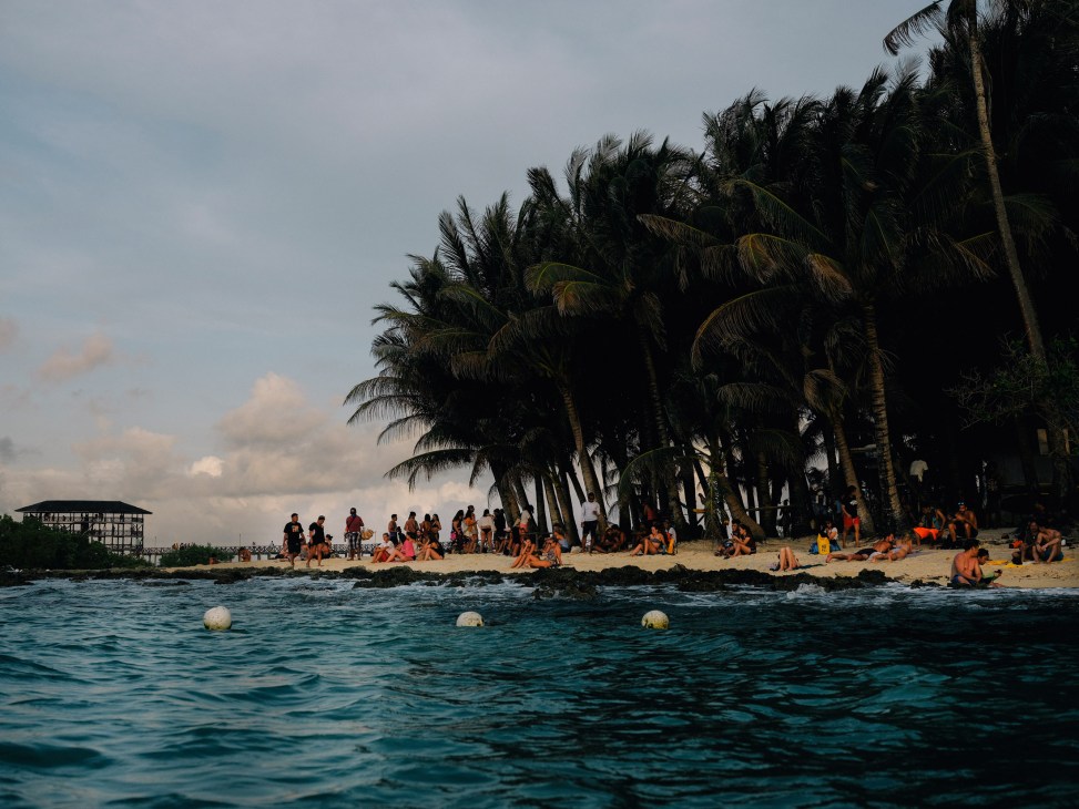 Beachgoers and palm trees at Cloud 9 surf break in Siargao, Philippines, viewed from the ocean.