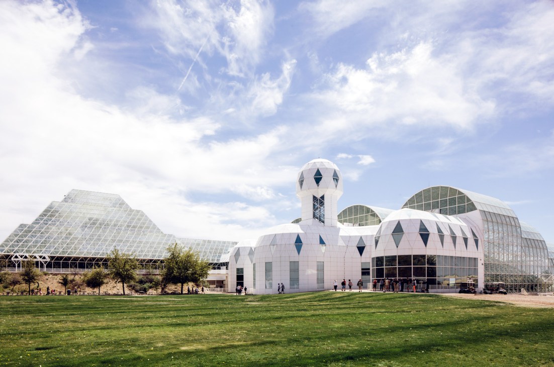 Biosphere 2 research facility with white structures and geodesic domes under blue sky.
