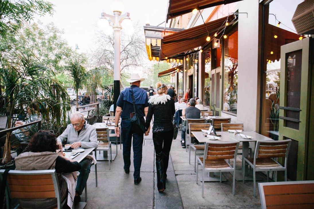 Outdoor patio dining area at Cup Café with diners seated at wooden tables under an orange awning.
