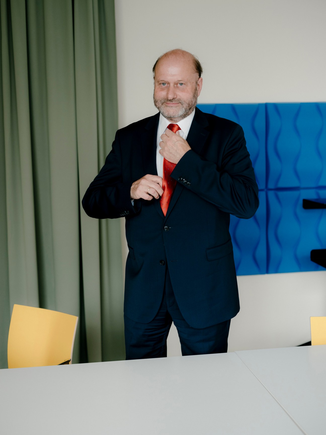 Herwig Wetzlinger, CEO of Vienna's Health Association, stands in a modern hospital corridor adjusting his red tie.
