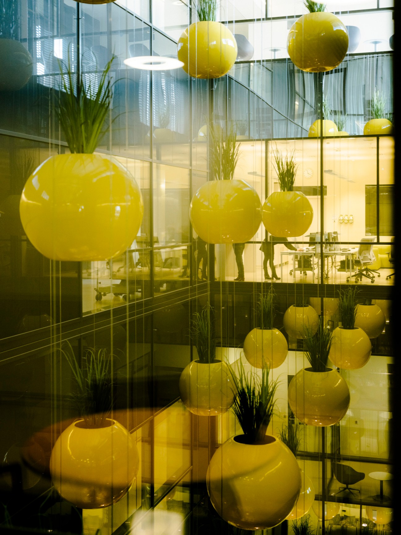 Hospital interior with yellow spherical planters containing plants suspended from ceiling and arranged on floor.