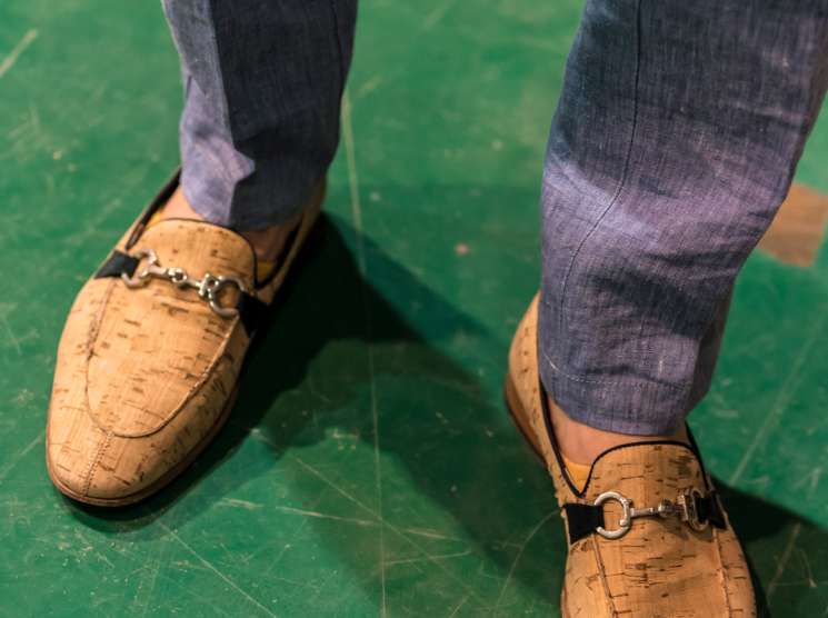 Cork-textured loafers with metal hardware worn with grey socks on a green floor.