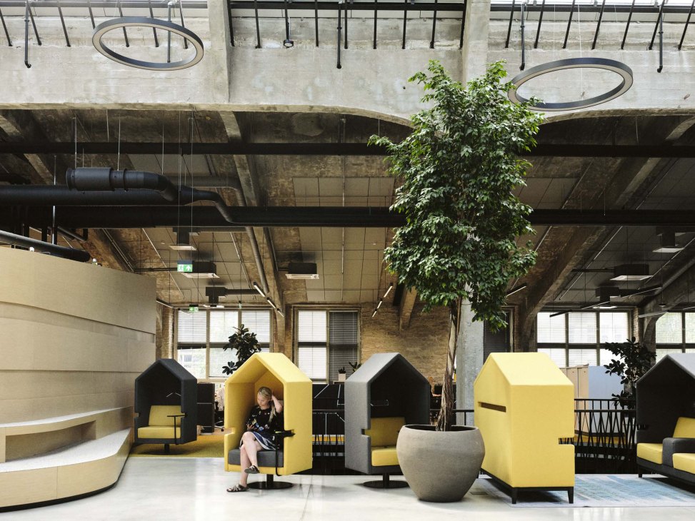 Yellow and black soundproofed chair pods in Aripaev newspaper office with concrete ceiling and skylights.