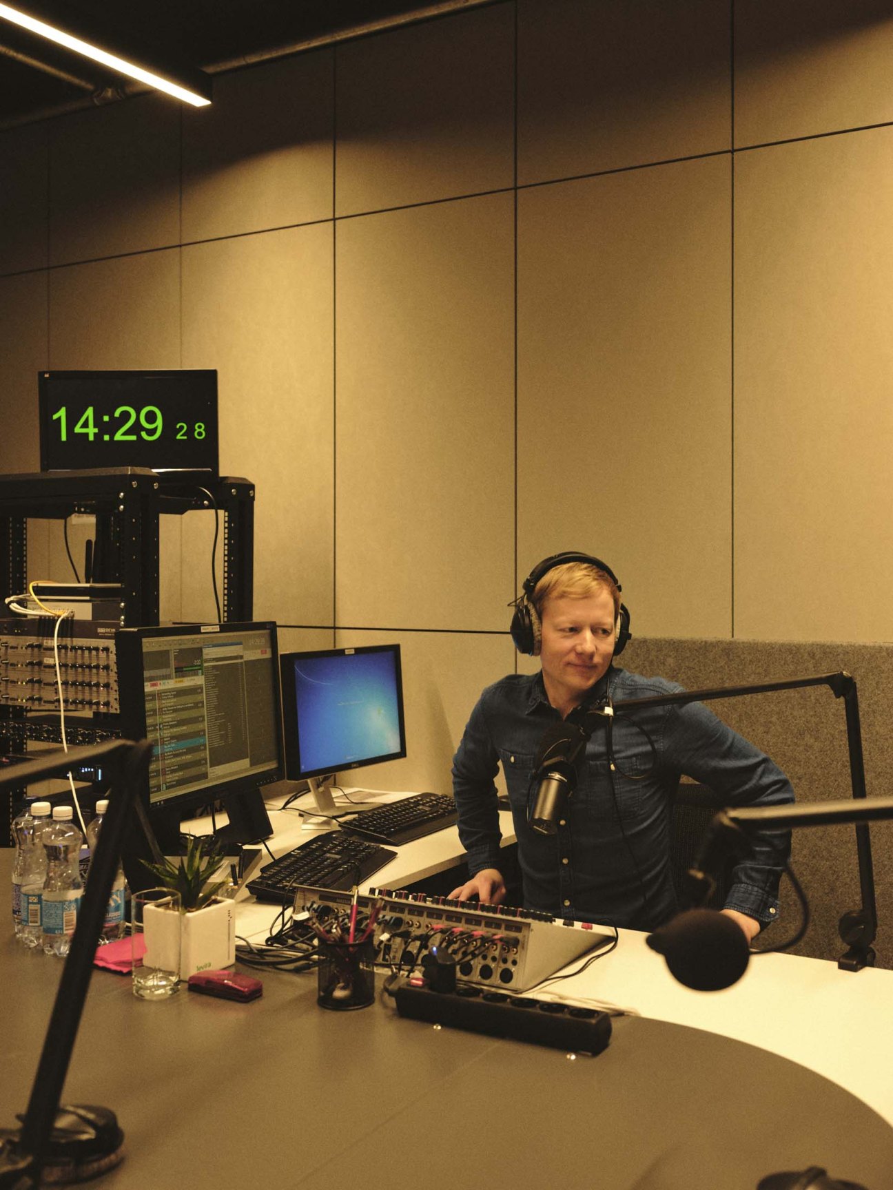 Editor and journalist Rivo Sarapik at a radio studio desk with broadcasting equipment and headphones.