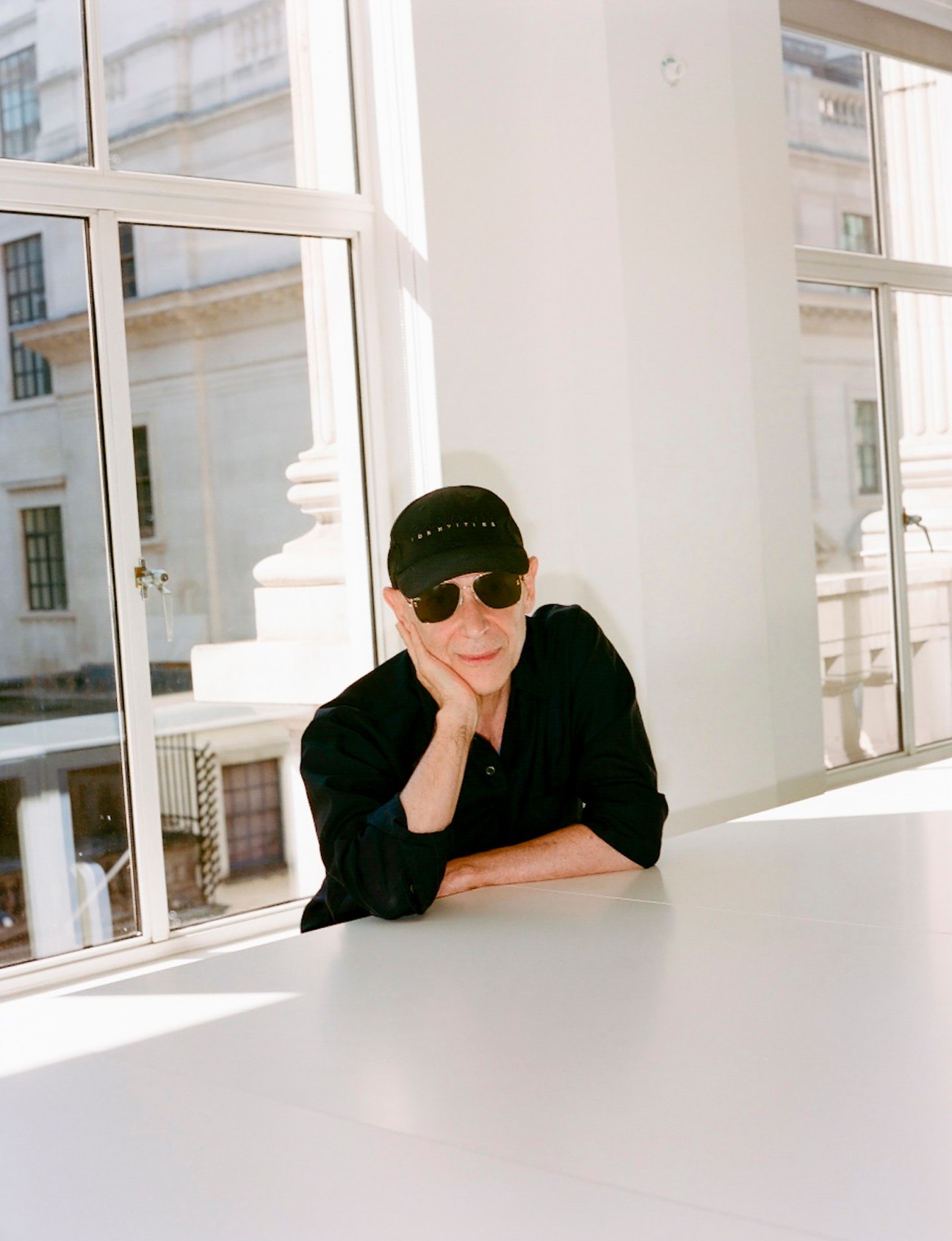 Adrian Joffe wearing black cap and sunglasses at white table by window in DSM London HQ.