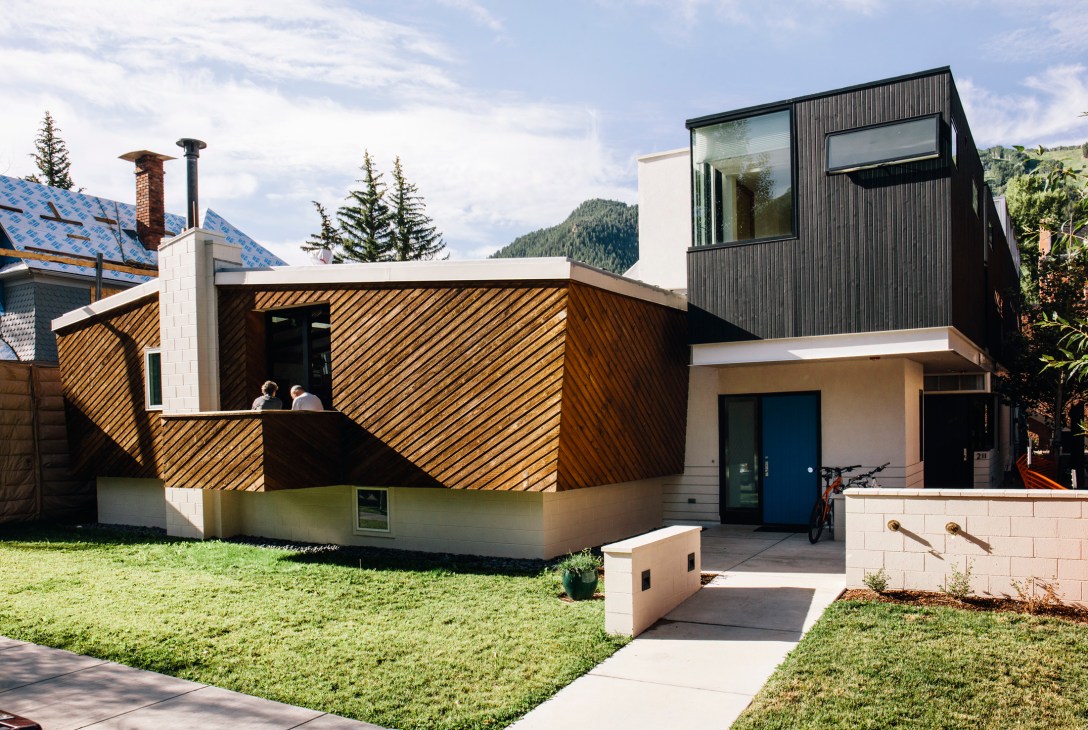 Modern residential home designed by architect Harry Teague with wooden siding and blue door against mountain backdrop.