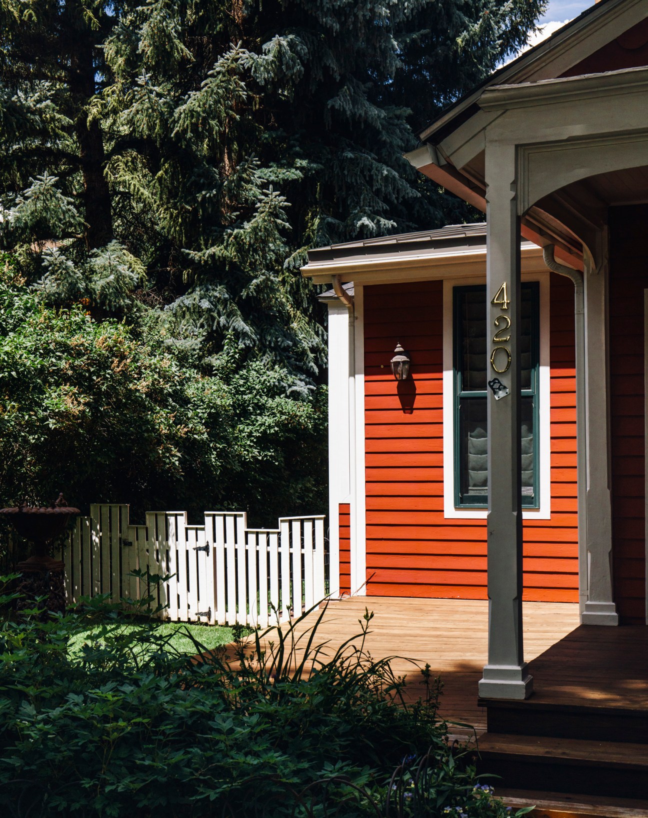Modern orange house with white trim and a white picket fence surrounded by evergreen trees.