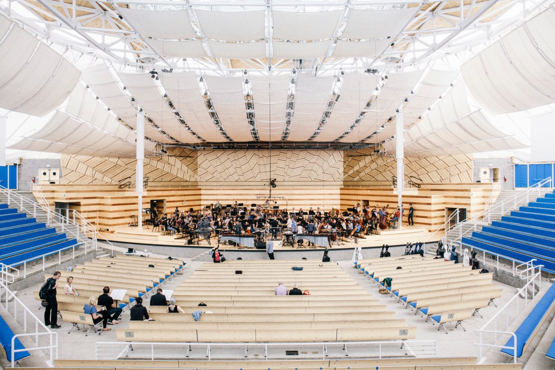 Interior of Benedict Music Tent with orchestra performing on stage under white tent roof with blue seating.