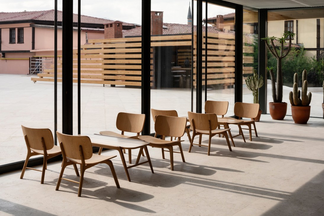 Wooden chairs designed by Kengo Kuma arranged on a sunny café terrace with timber and glass architecture in the background.