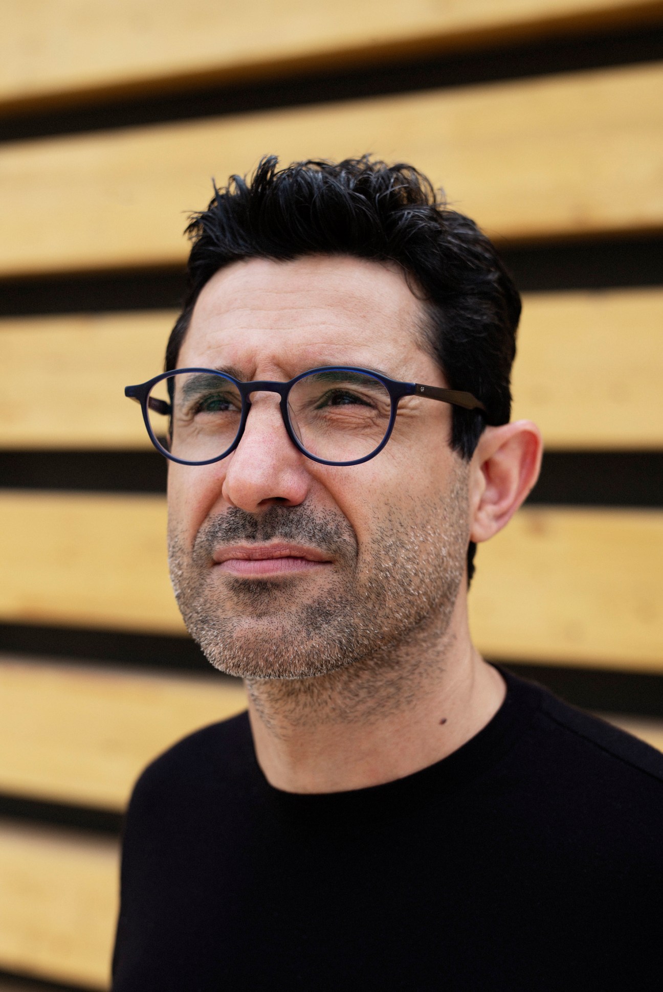 Portrait of Ozay Yakak, construction co-ordinator at Polimeks, wearing glasses against a yellow wooden background.