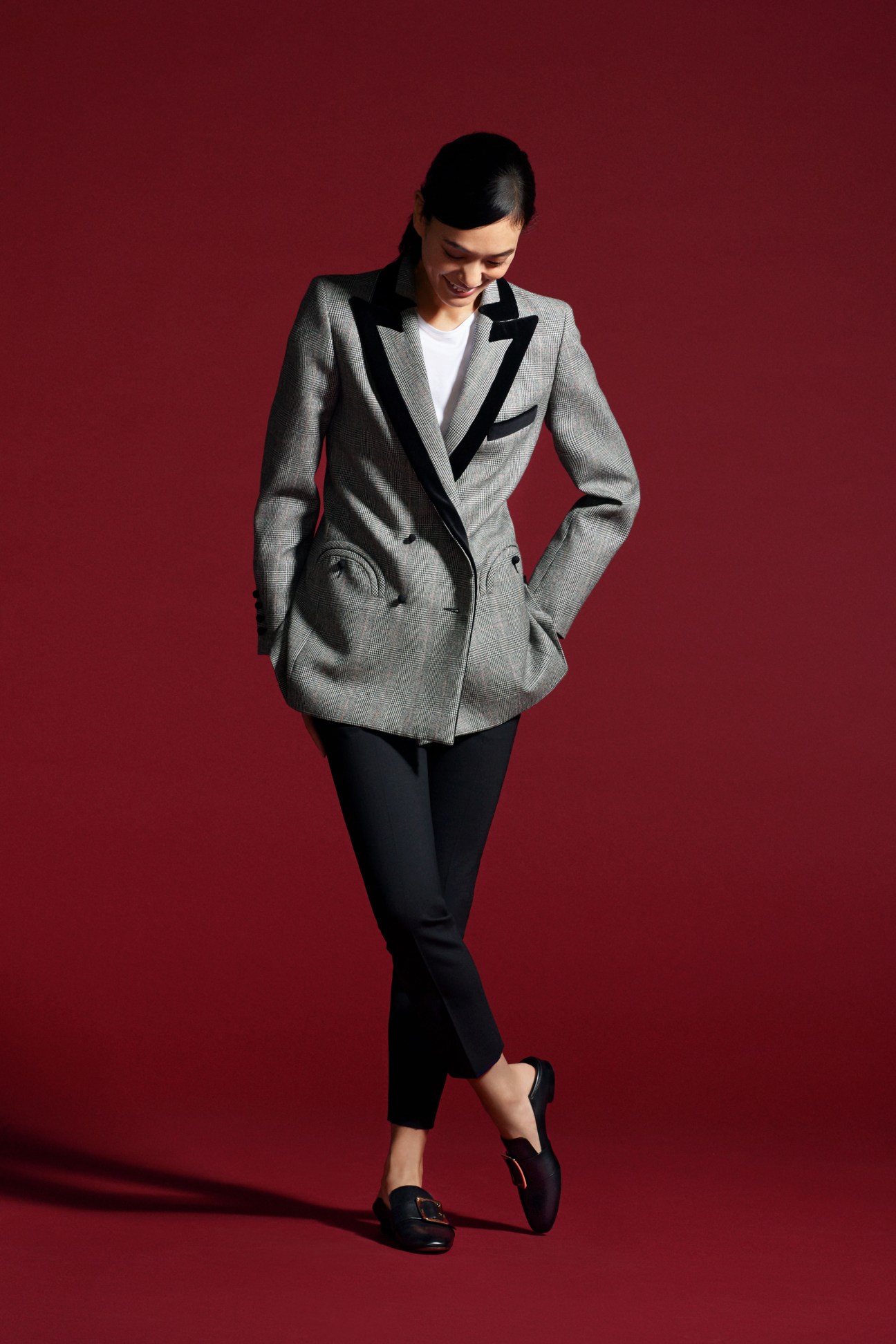 Woman in grey blazer with black lapels, white t-shirt, and black trousers on red background