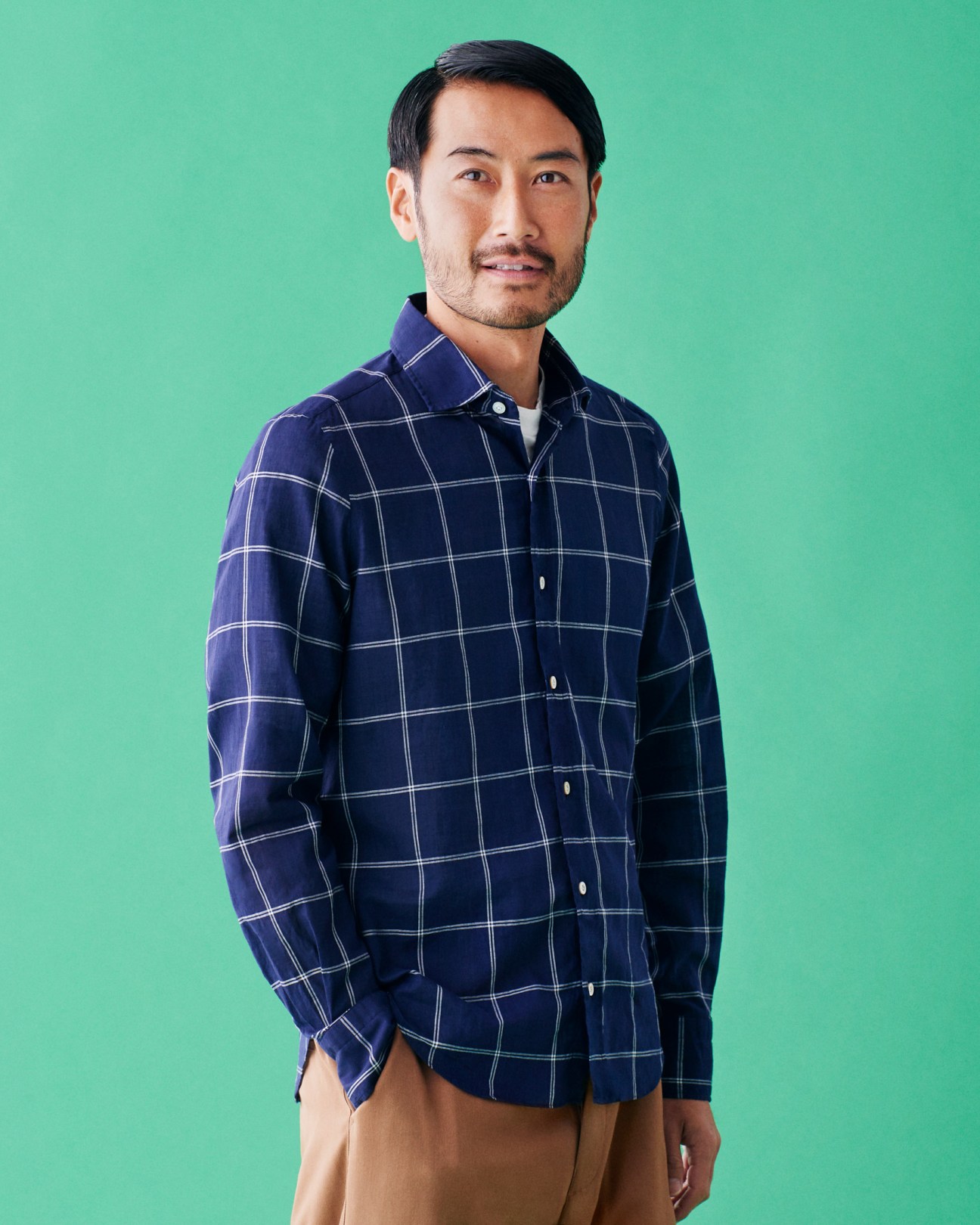 Man wearing navy plaid shirt by Finamore with Unfil t-shirt and Barena trousers against green background