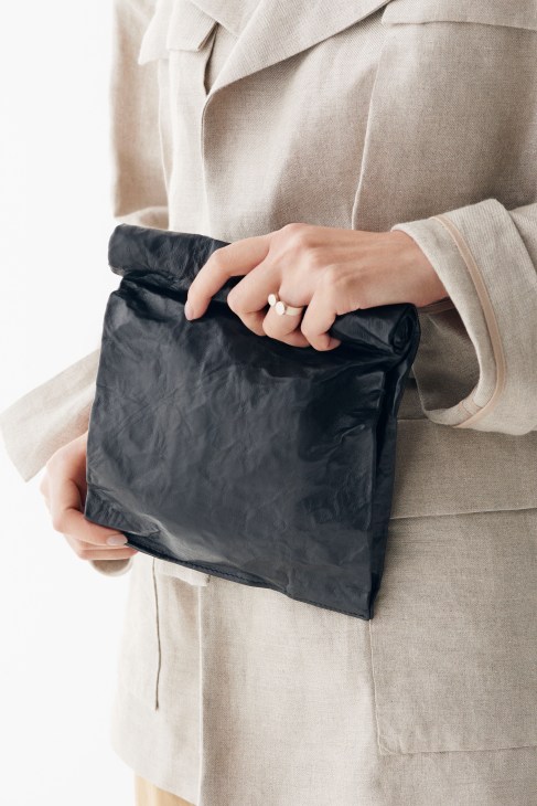 Person wearing a beige jacket holding a black crinkled bag by Zilla with a pearl ring visible.