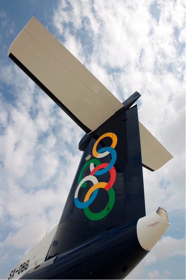 Olympic Air aircraft tail fin displaying the airline's colorful interlocking rings logo against sky.