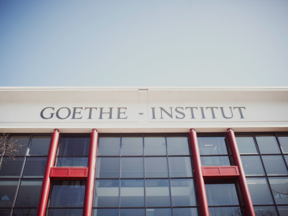 The main entrance of the Goethe-Institut in Munich with red pillars and signage on white facade.